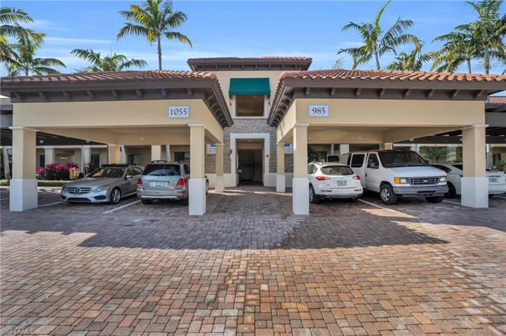 View front of complex with a tiled roof, stucco siding, stone siding, and covered parking