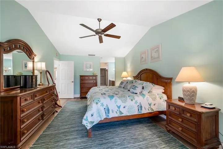 Bedroom with lofted ceiling, a ceiling fan, ensuite bathroom, and dark wood-style flooring
