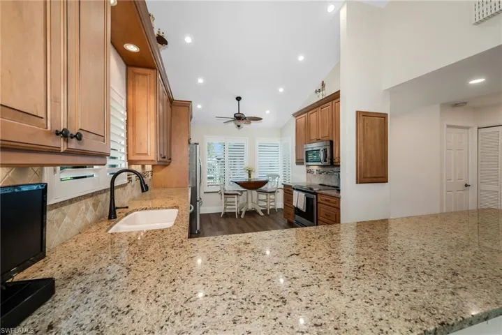 Kitchen with light stone countertops, stainless steel appliances, wood finish cabinetry, a ceiling fan, and vaulted ceiling