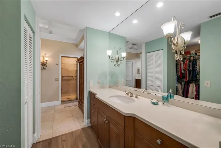 Full bath featuring vanity, a spacious closet, light wood finished floors, suspended lighting, and a stall shower