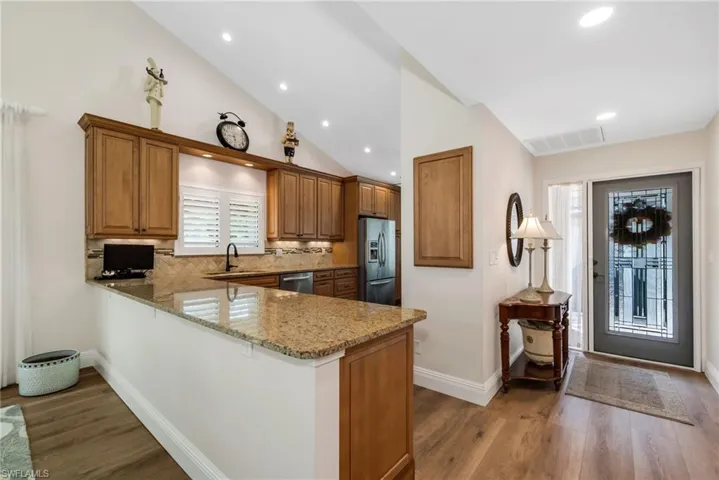 Kitchen featuring light stone counters, a peninsula, wood finish cabinets, backsplash, and stainless steel appliances