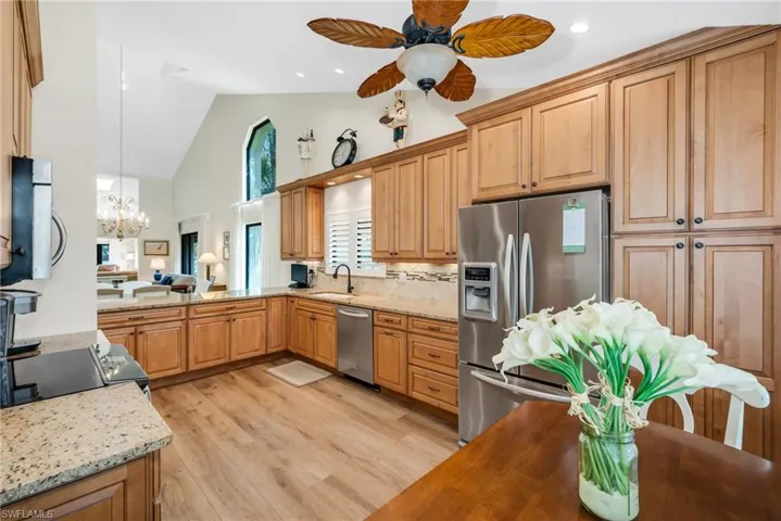 Kitchen with stainless steel appliances, light stone countertops, hanging lights, light wood finished floors, and vaulted ceiling