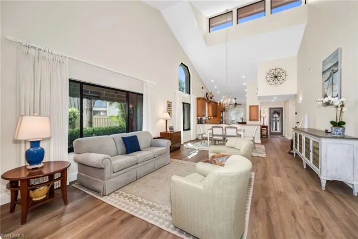 Living area with light wood-style floors, hanging lights, and a high ceiling