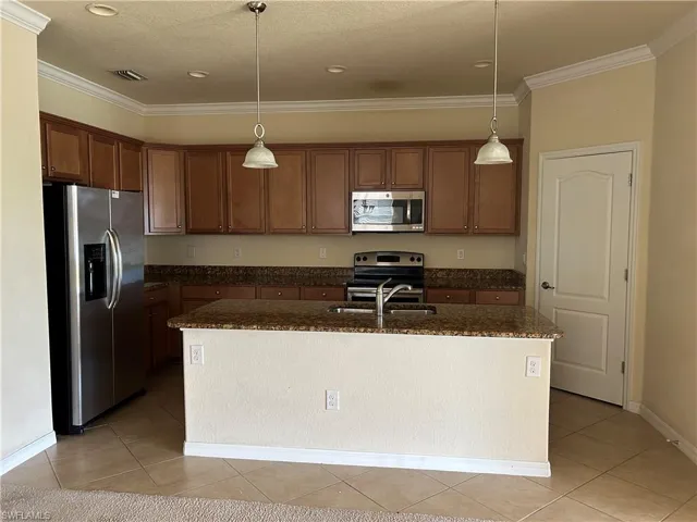 Kitchen with dark stone countertops, stainless steel appliances, decorative light fixtures, a kitchen island with sink, and crown molding