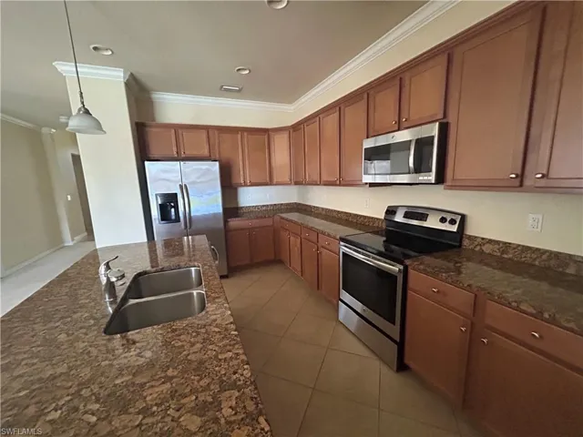 Kitchen featuring stainless steel appliances, wood finish cabinetry, dark stone counters, crown molding, and decorative light fixtures