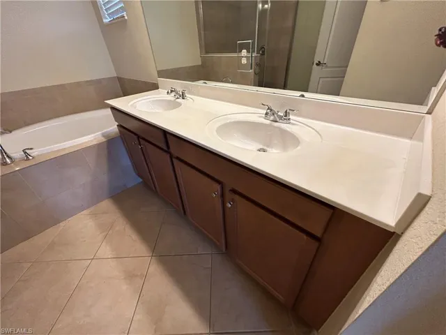 Full bath with double vanity, a bath, and light tile patterned floors