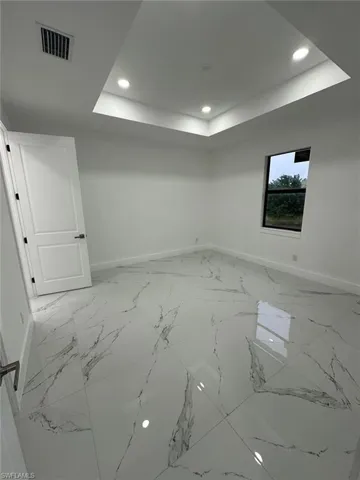 Spare room featuring recessed lighting, light marble finish floors, and a tray ceiling