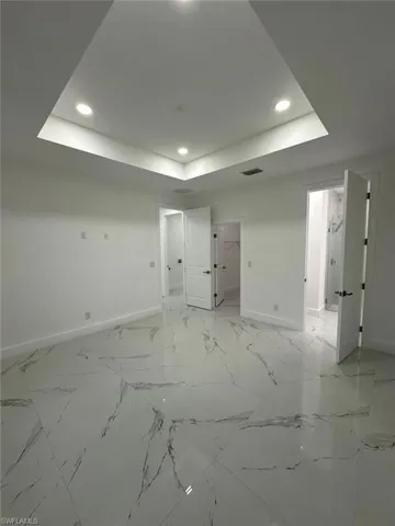 Unfurnished room with a raised ceiling, recessed lighting, and light marble finish floors