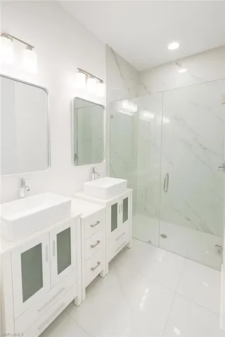 Bathroom featuring two vanities, a marble finish shower, and recessed lighting