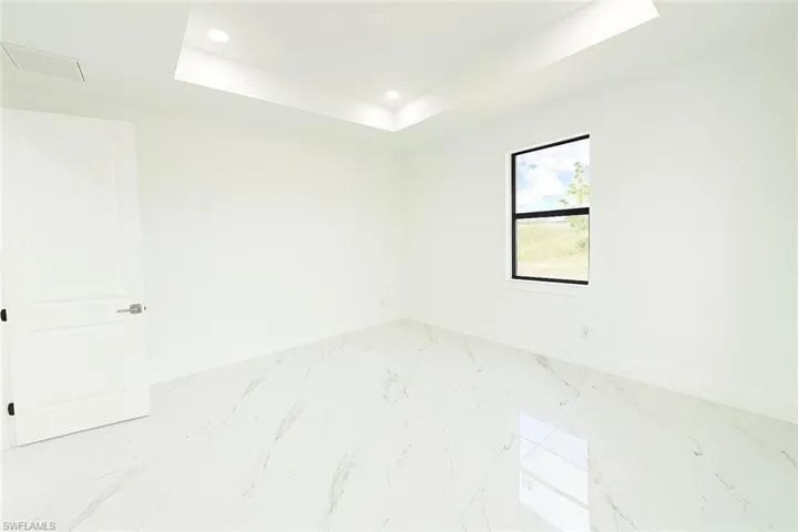 Empty room featuring a tray ceiling, light marble finish floors, and recessed lighting