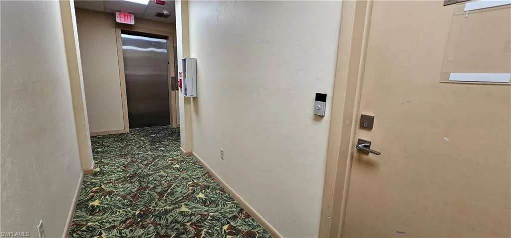 Hall with elevator, a textured wall, and carpet flooring