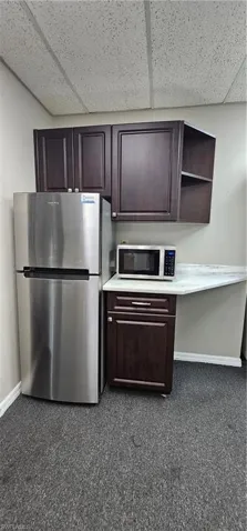 Kitchen with refrigerator, light countertops, a drop ceiling, white microwave, and dark wood finish cabinetry