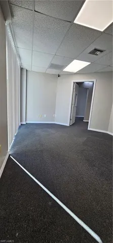 Spare room with a drop ceiling and dark colored carpet