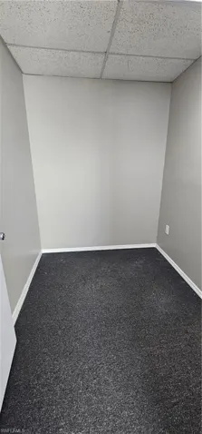 Empty room with a paneled ceiling and dark colored carpet
