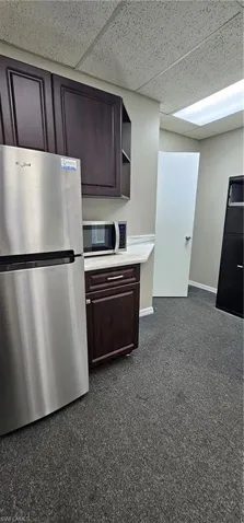 Kitchen featuring freestanding refrigerator, a drop ceiling, open shelves, light countertops, and dark wood finish cabinets