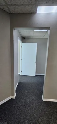 Hall featuring a paneled ceiling, dark carpet, and a textured wall