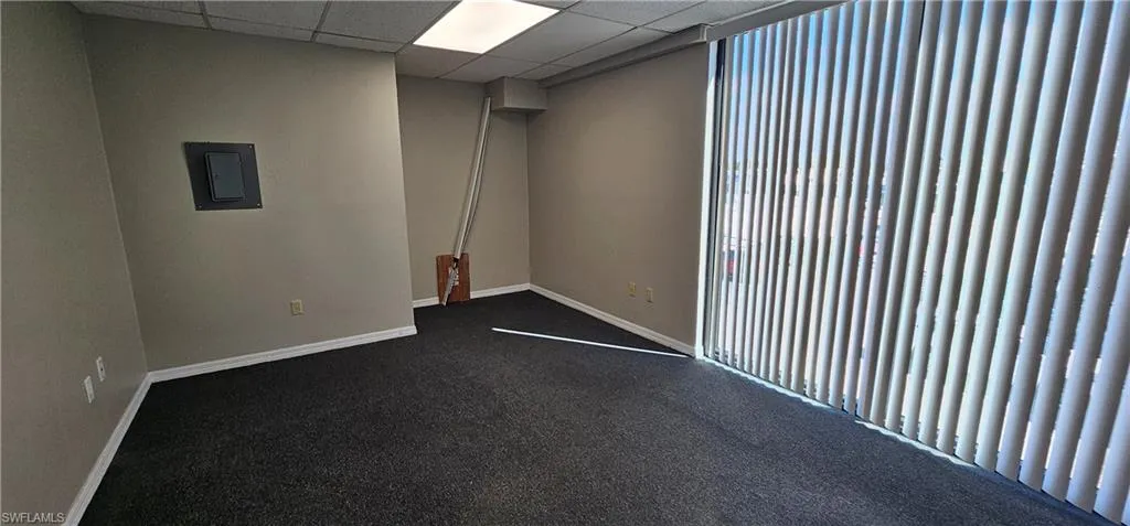 Empty room featuring a paneled ceiling, dark carpet, and electric panel