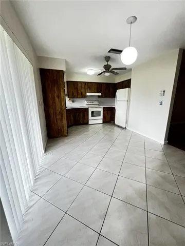 Kitchen featuring dark wood finish cabinetry, white appliances, light countertops, light tile patterned flooring, and decorative light fixtures