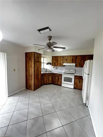 Kitchen featuring light countertops, white appliances, light tile patterned flooring, a ceiling fan, and wood finish cabinets