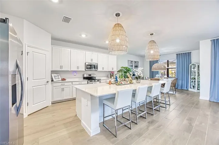 Kitchen with light wood finished floors, stainless steel appliances, white cabinetry, a large island with sink, and a breakfast bar