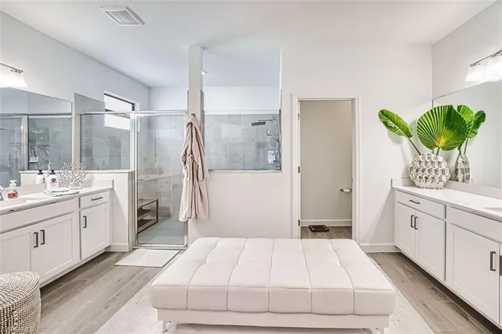 Bathroom featuring wood finish floors, two vanities, and a shower stall