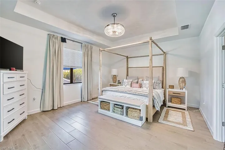 Bedroom featuring a tray ceiling, suspended lighting, and light wood-type flooring