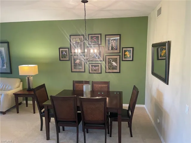 Carpeted dining space with a chandelier, visible vents, and baseboards