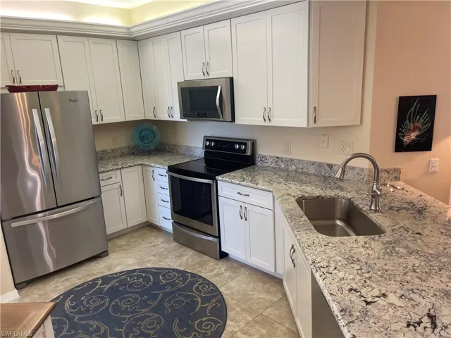 Kitchen with light tile patterned floors, appliances with stainless steel finishes, light stone counters, white cabinetry, and a sink