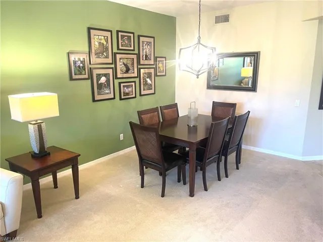 Dining room featuring light carpet, baseboards, visible vents, and a notable chandelier