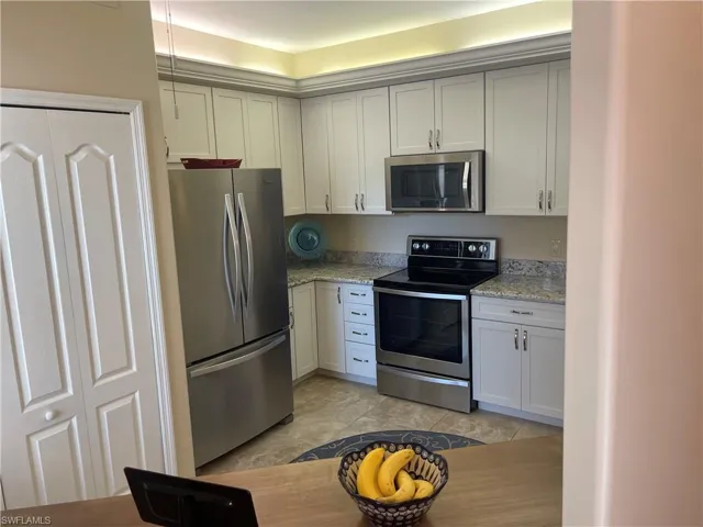 Kitchen featuring appliances with stainless steel finishes, light stone counters, and white cabinetry