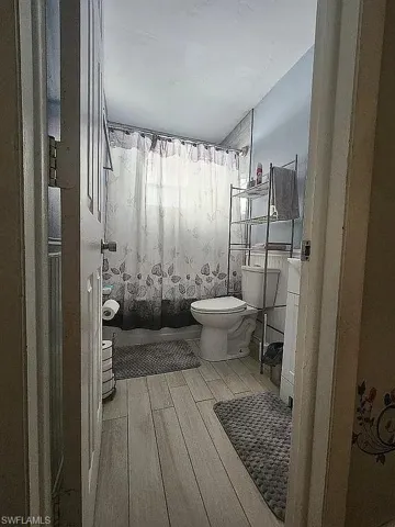 Bathroom with shower / bathtub combination with curtain, toilet, and wood finished floors