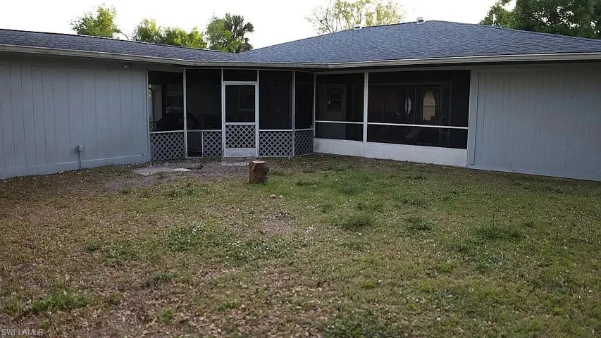 Back of property featuring a lawn, a shingled roof, and a sunroom