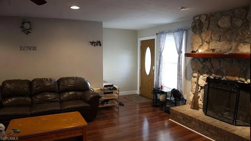 Living area featuring baseboards, a stone fireplace, and wood finished floors