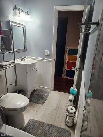Bathroom featuring vanity, toilet, wood finished floors, and a wainscoted wall