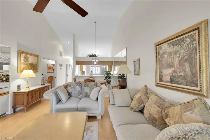Living room with high vaulted ceiling, light wood-style flooring, a chandelier, and ceiling fan