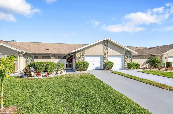 View of front facade featuring a front yard, stone siding, concrete driveway, and a garage