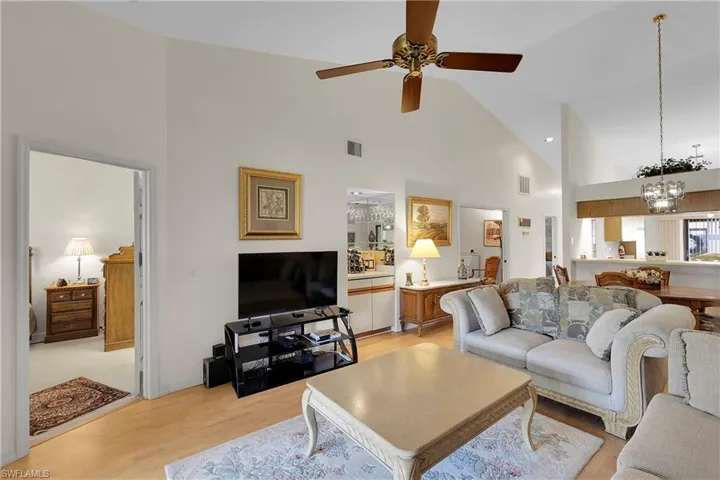 Living area with high vaulted ceiling, light wood-type flooring, a ceiling fan, and a chandelier