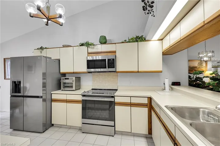 Kitchen with a chandelier, decorative light fixtures, stainless steel appliances, light countertops, and high vaulted ceiling