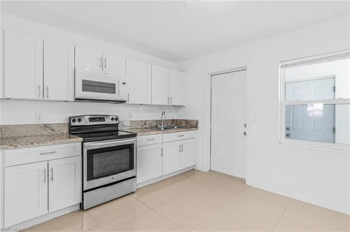 Kitchen with stainless steel electric range oven, white microwave, light stone counters, and white cabinetry
