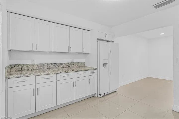 Kitchen featuring white fridge with ice dispenser, light stone countertops, white cabinets, and light marble finish flooring