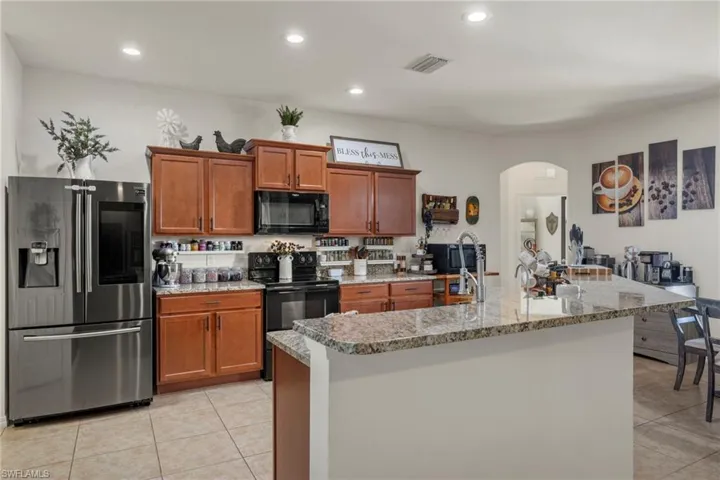 Kitchen with light tile patterned floors, light stone counters, a kitchen island with sink, and black appliances
