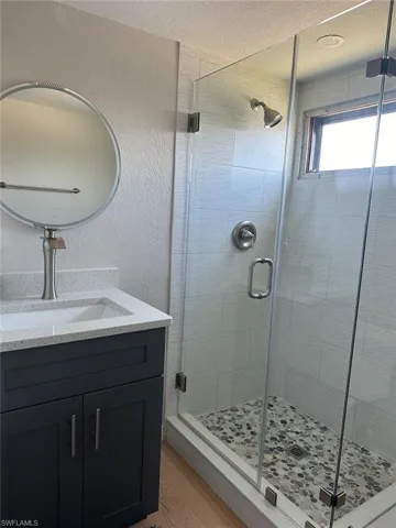 Bathroom featuring a shower with shower door, vanity, and a textured ceiling