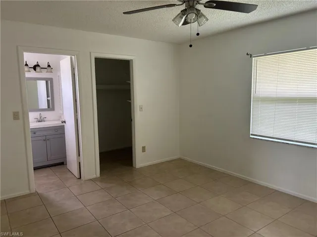 Unfurnished bedroom featuring a spacious closet, light tile patterned floors, a textured ceiling, ensuite bath, and ceiling fan