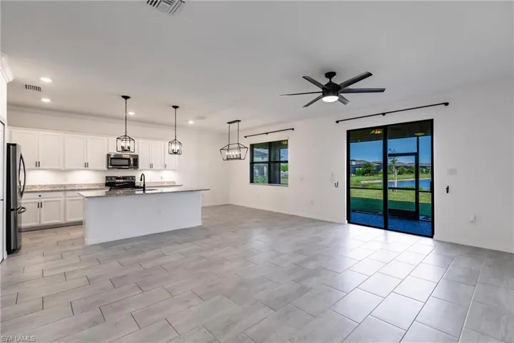 Kitchen with stainless steel appliances, ceiling fan, decorative light fixtures, a center island with sink, and white cabinets