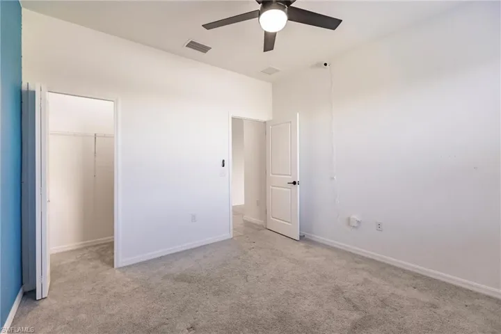 Unfurnished bedroom featuring light carpet, a walk in closet, a closet, and ceiling fan