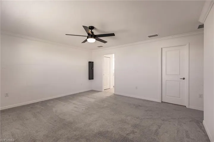 Unfurnished room featuring electric panel, crown molding, ceiling fan, and light colored carpet