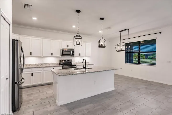 Kitchen with appliances with stainless steel finishes, decorative light fixtures, white cabinetry, and a kitchen island with sink