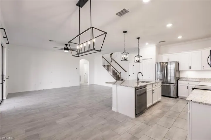 Kitchen featuring hanging light fixtures, appliances with stainless steel finishes, a center island with sink, white cabinets, and ornamental molding
