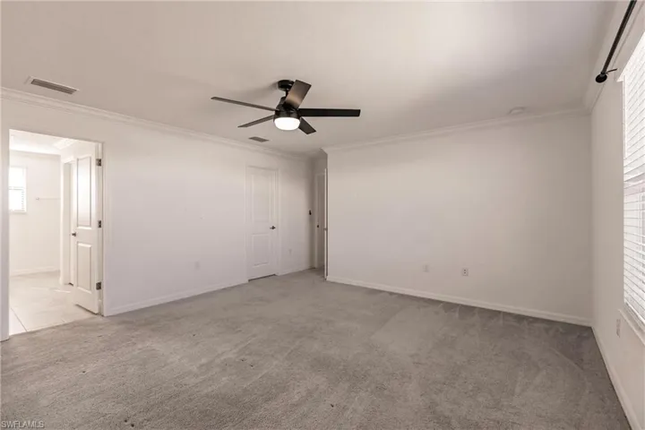 Empty room featuring ceiling fan, light colored carpet, and ornamental molding