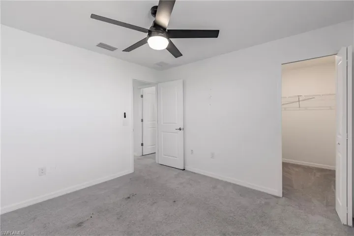 Unfurnished bedroom featuring a closet, light colored carpet, a spacious closet, and ceiling fan